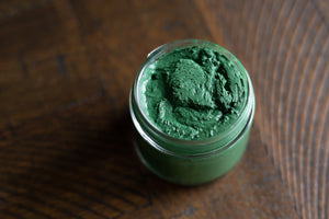 top view of uncapped glass jar of green spirulina face mask on wooden table