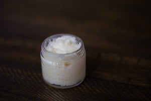 2 oz glass jar of coconut scrub sitting atop a wooden table