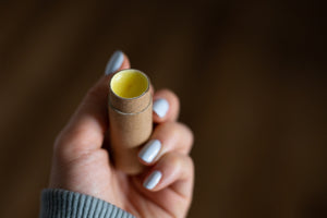 Hand holding a cardboard tube of peppermint lip balm with the cap removed