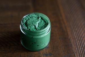 uncapped glass jar of green spirulina face mask on wooden table