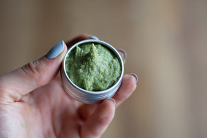 hand holding uncapped metal tin of green matcha mint sugar scrub in 1/2 oz size